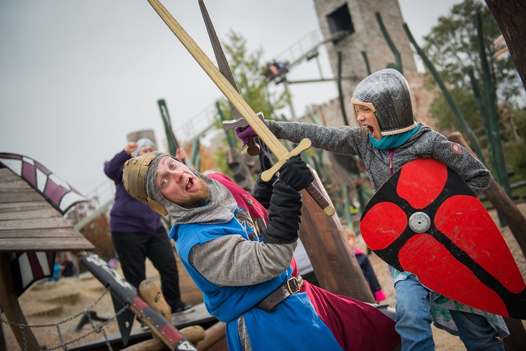 Als Ritter verkleideter Schausteller kämpft mit Holzschwert gegen ein Kind mit Schwert und Schild